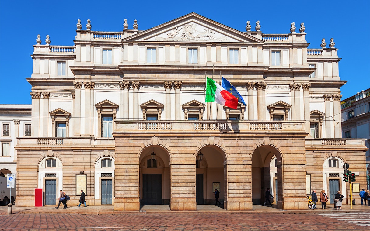 La Scala Opera House in Milan with Italian and EU flags.