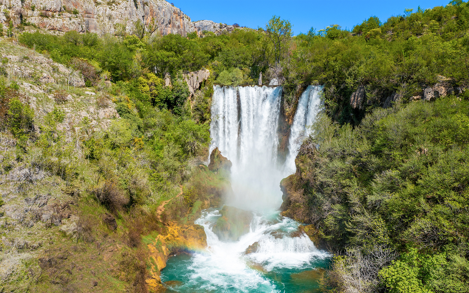 Aerial view of Manojlovac waterfall cascading through lush greenery in Krka National Park, Croatia.