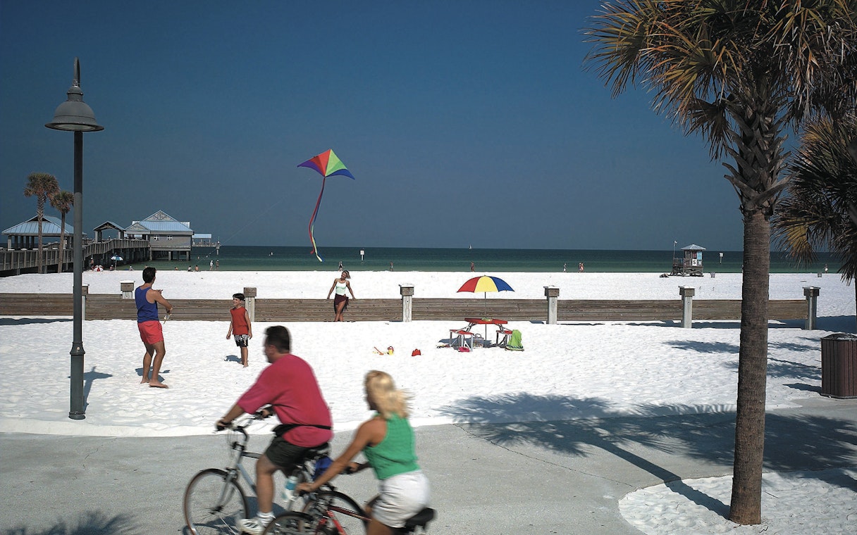 Clearwater Beach with people biking and flying a kite near the pier.