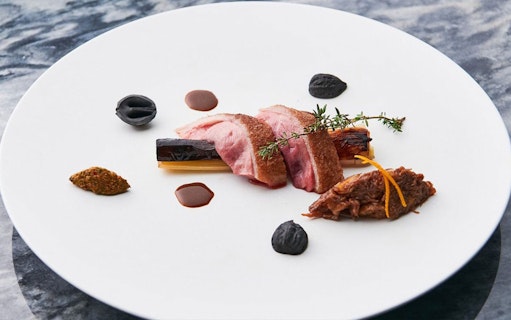 Wagyu beef slices with garnishes on a white plate, part of a special course.