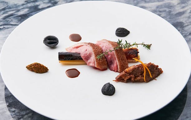 Wagyu beef slices with garnishes on a white plate, part of a special course.