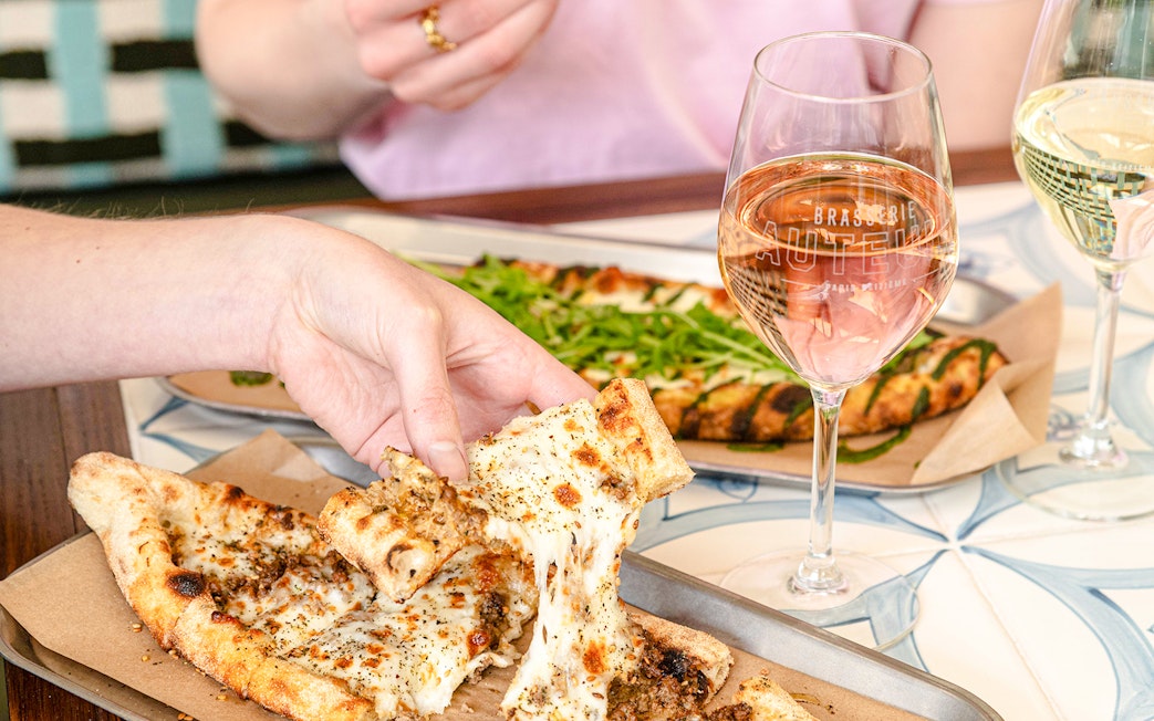 Pizza being shared at Brasserie Auteuil with glasses of wine.