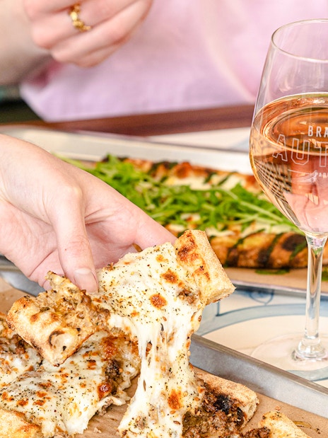 Pizza being shared at Brasserie Auteuil with glasses of wine.