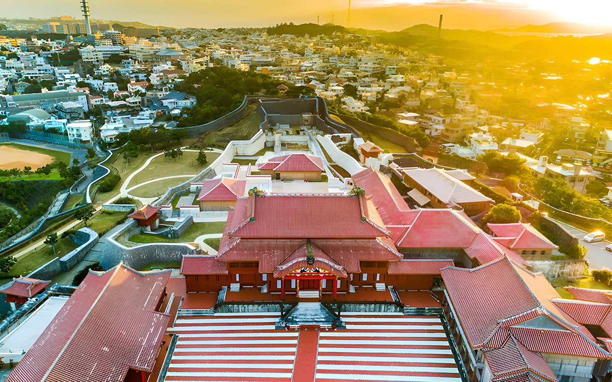 Aerial view of Shurijo Castle Park in Okinawa at sunset, showcasing traditional red-roofed architecture.
