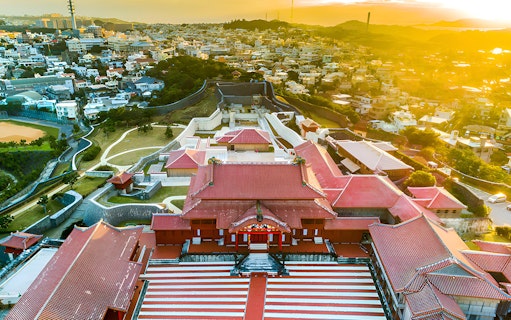 Aerial view of Shurijo Castle Park in Okinawa at sunset, showcasing traditional red-roofed architecture.