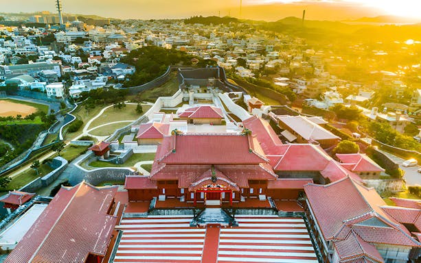 Aerial view of Shurijo Castle Park in Okinawa at sunset, showcasing traditional red-roofed architecture.