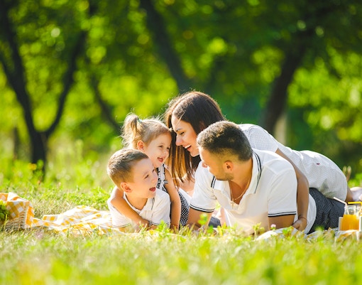 Family enjoying picnic in countryside, parents dining with children outdoors.
