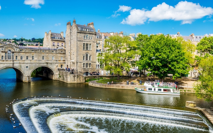 Historic Bath city street with tour group near Pulteney Bridge, live music performance nearby.