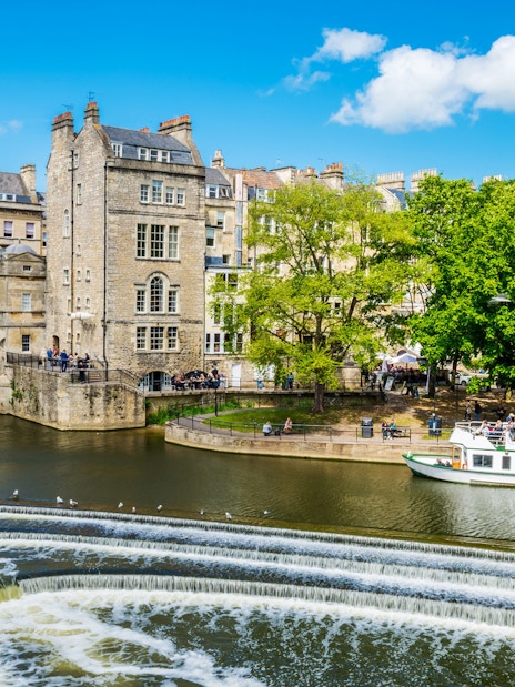 Historic Bath city street with tour group near Pulteney Bridge, live music performance nearby.