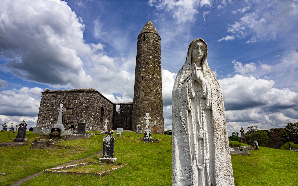 Glendalough Monastic Site with round tower and statue in a historic cemetery.