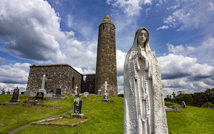 Glendalough Monastic Site with round tower and statue in a historic cemetery.