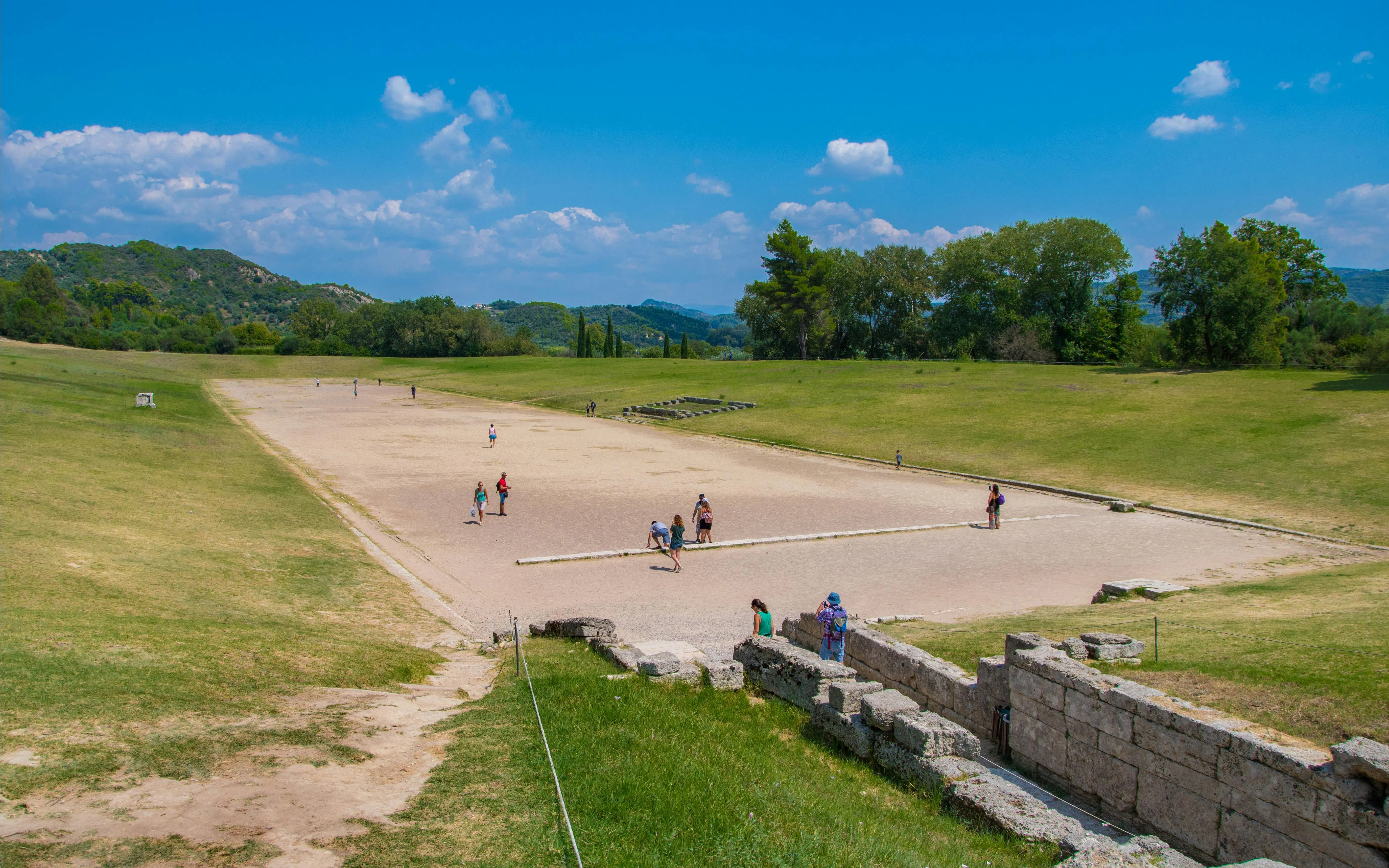 Stadium at the Archaeological Site of Olympia, Greece, with visitors exploring the ancient track.