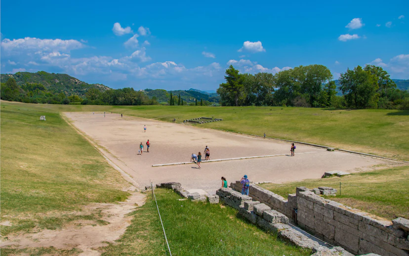 Stadium at the Archaeological Site of Olympia, Greece, with visitors exploring the ancient track.