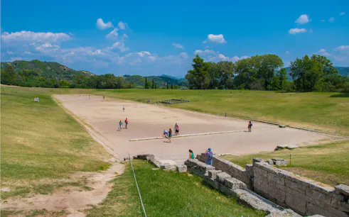 Stadium at the Archaeological Site of Olympia, Greece, with visitors exploring the ancient track.