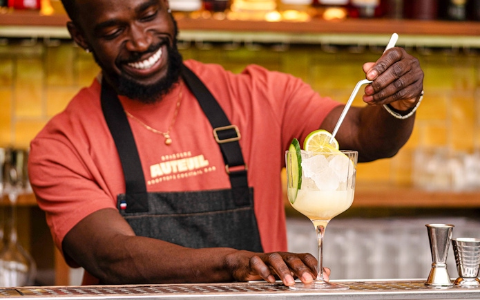 Waiter preparing cocktail with lime and cucumber garnish at Brasserie Auteuil.