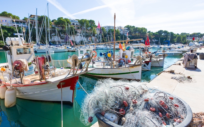 Fishing boats docked at Porto Cristo marina, Mallorca, with nets in the foreground.