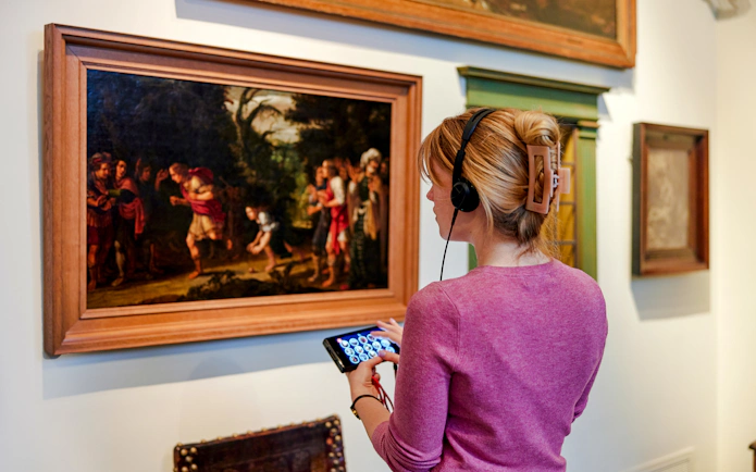 Visitor with audio guide viewing painting at Rembrandt House Museum, Amsterdam.