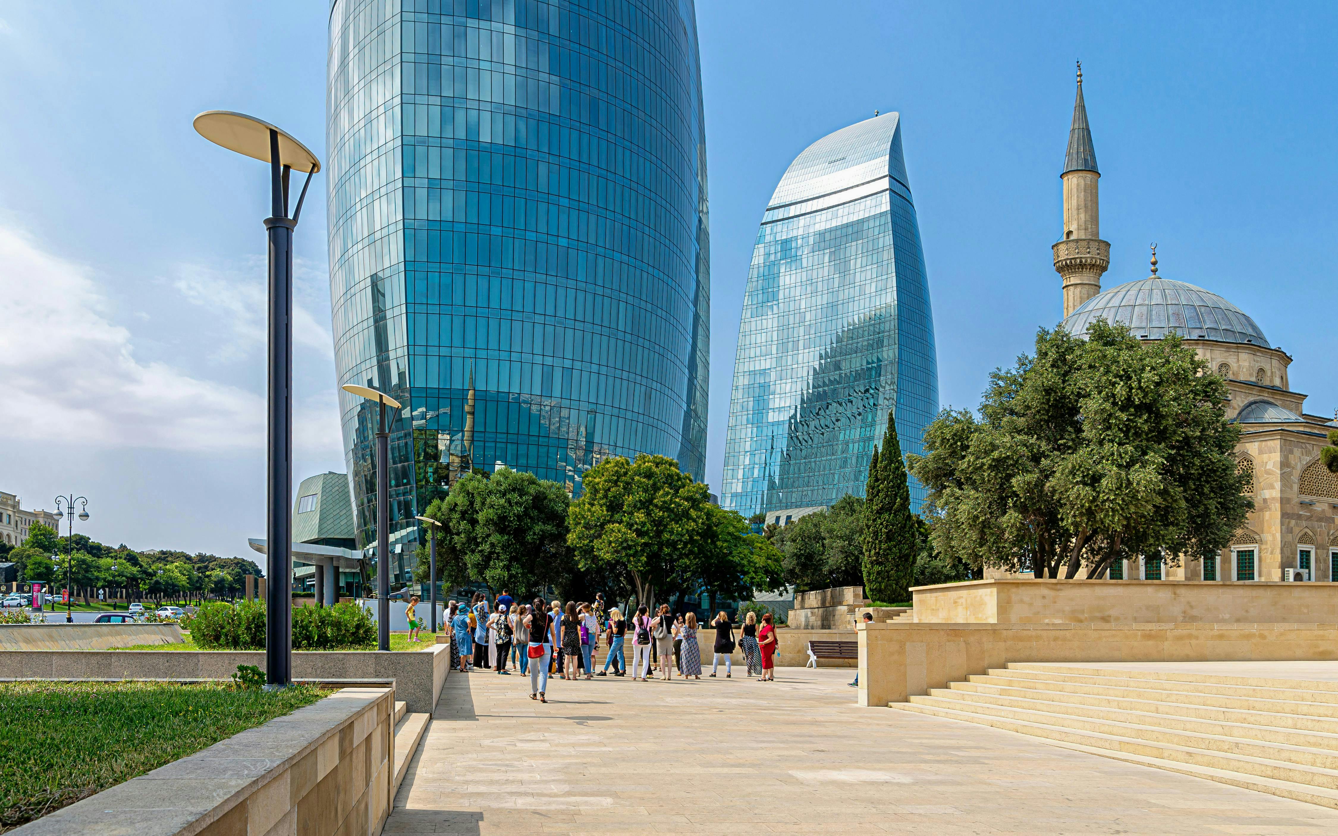 Flame Towers complex in Baku with nearby mosque and tourists exploring.