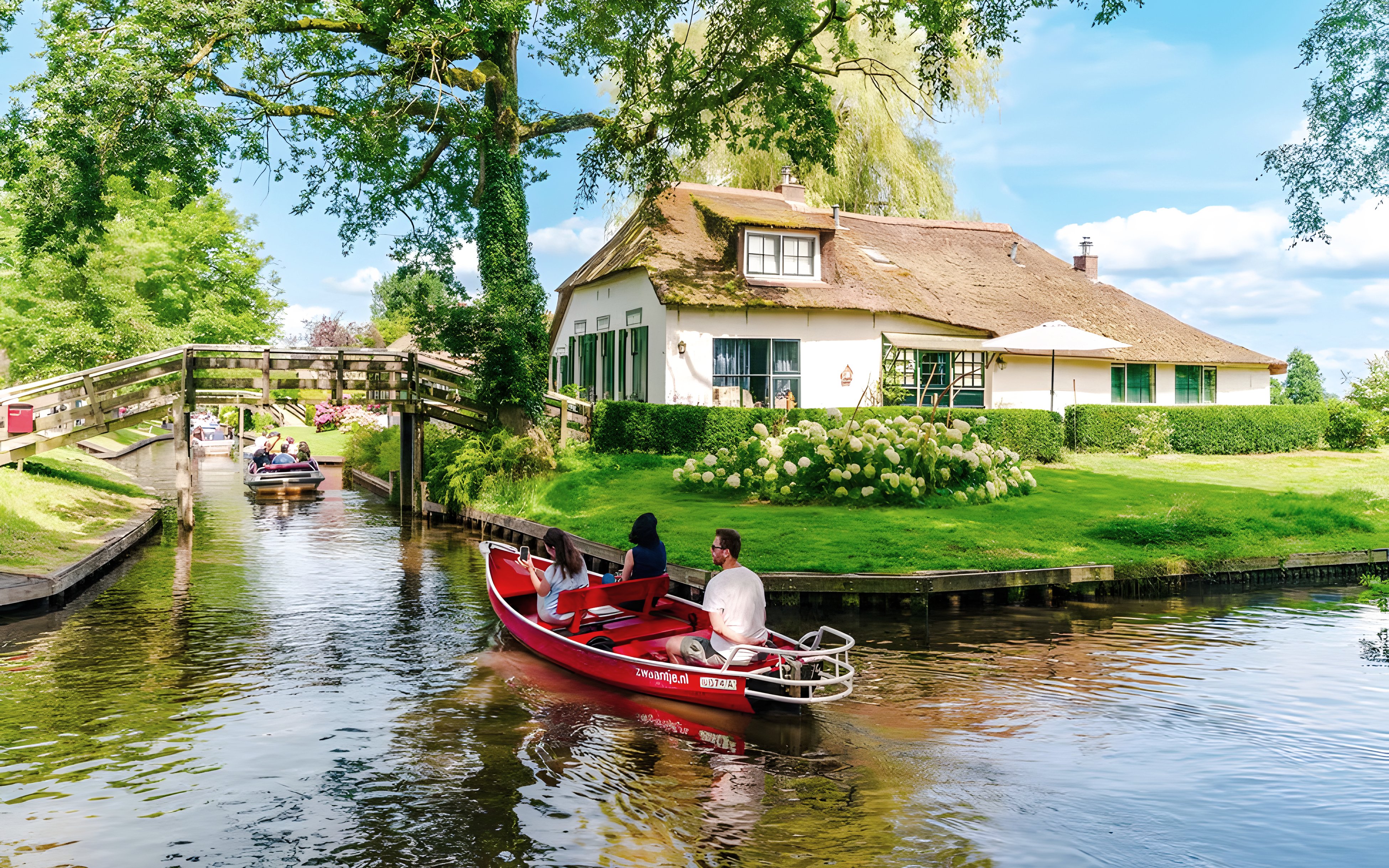Guests on a boat ride through Giethoorn's canals, passing a traditional Dutch house and wooden bridge.