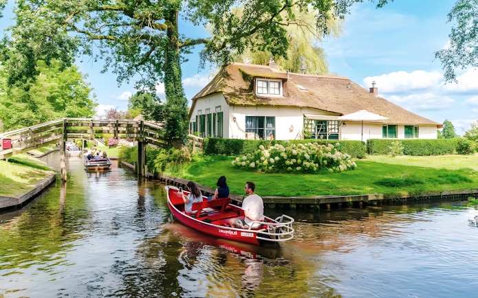 Guests on a boat ride through Giethoorn's canals, passing a traditional Dutch house and wooden bridge.