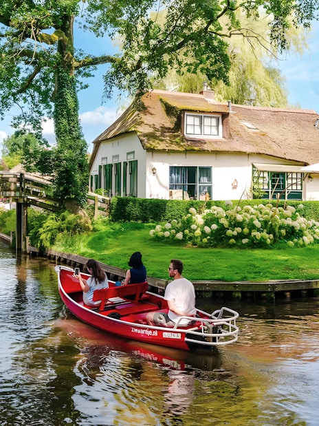Guests on a boat ride through Giethoorn's canals, passing a traditional Dutch house and wooden bridge.