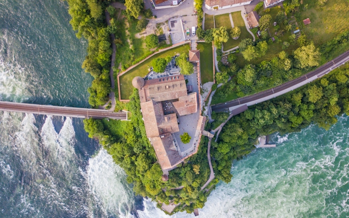 Aerial view of Schloss Laufen Castle surrounded by Rhine Falls and lush greenery.