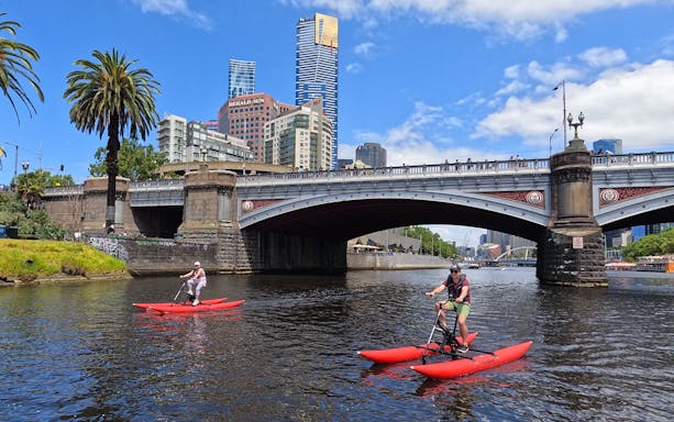 People riding waterbikes on Yarra River near a bridge in Melbourne, Australia.