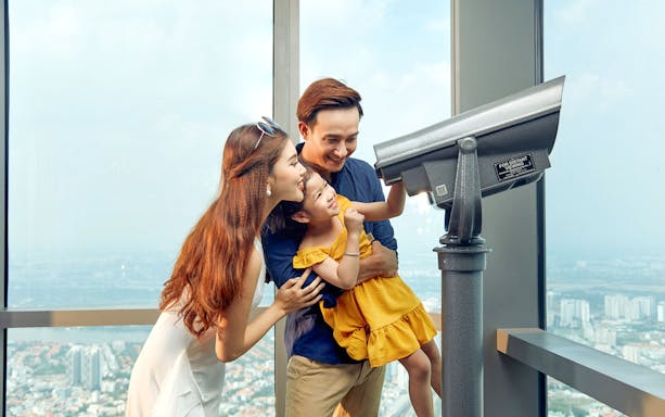Family enjoying the view through a telescope at Saigon Skydeck, Bitexco Financial Tower.