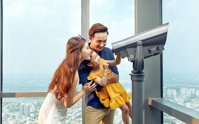 Family enjoying the view through a telescope at Saigon Skydeck, Bitexco Financial Tower.