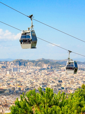 Montjuic Cable Car over Barcelona cityscape with distant mountains.