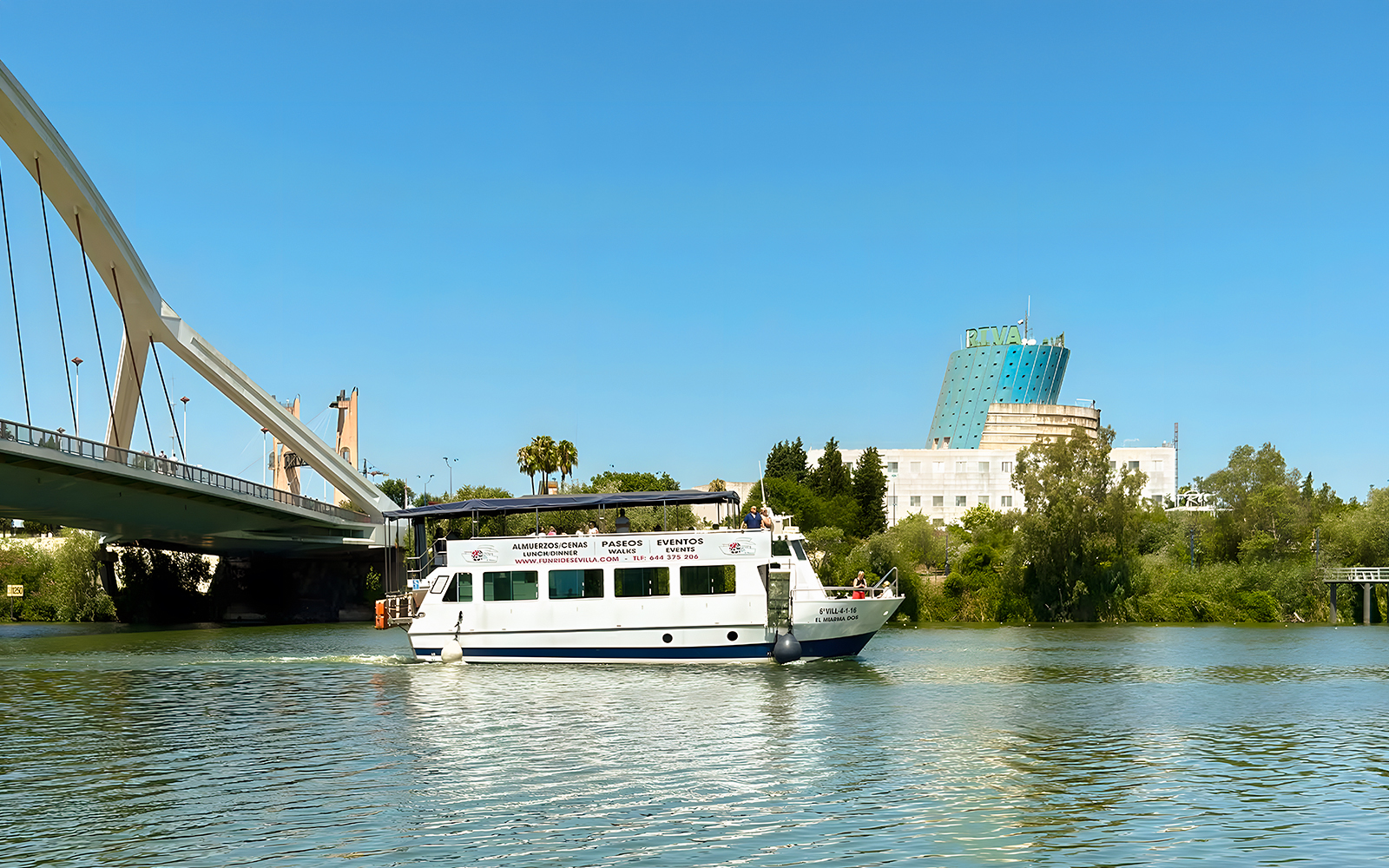 Sightseeing cruise boat on Guadalquivir River near bridge in Seville, Spain.