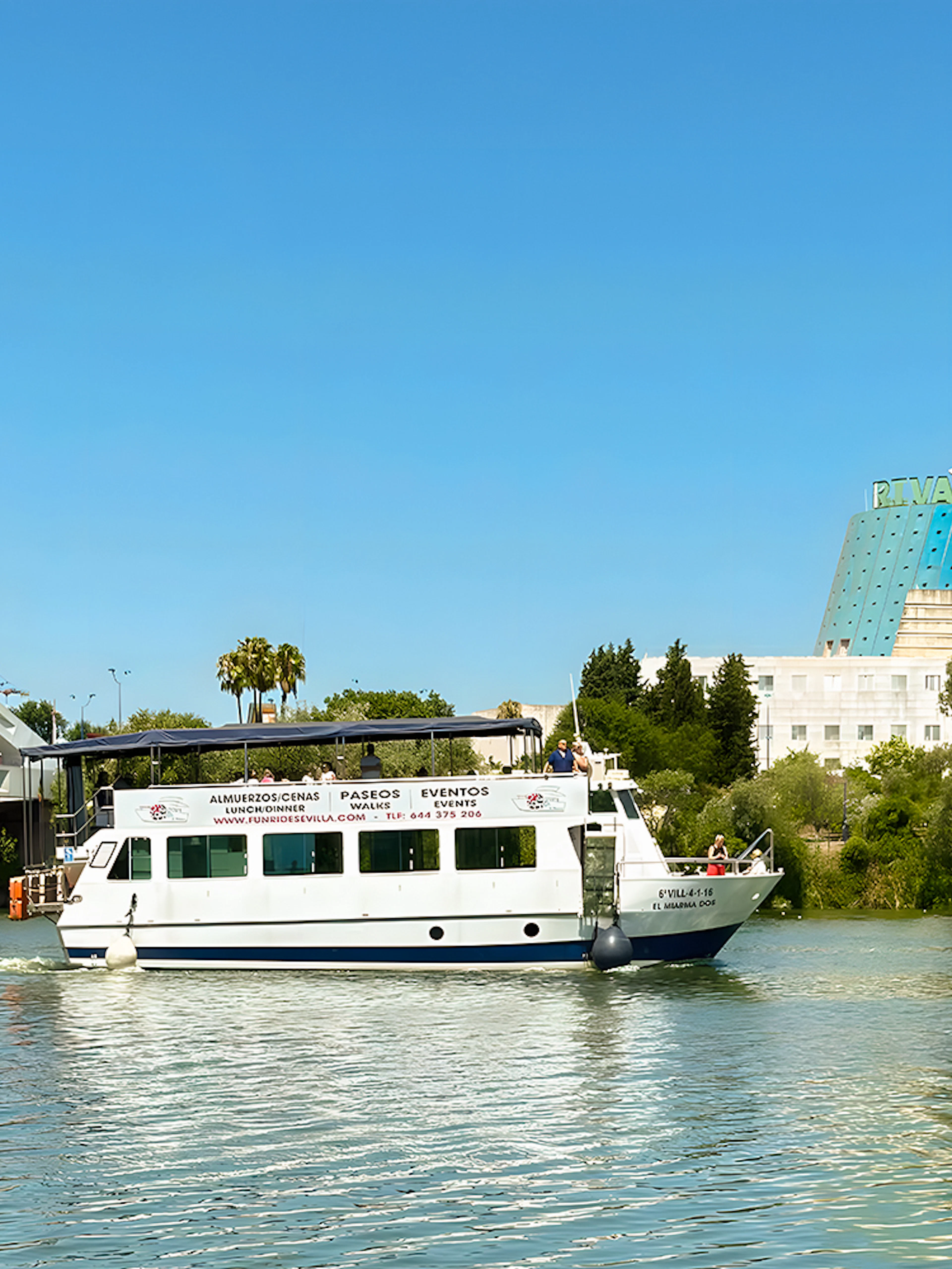 Sightseeing cruise boat on Guadalquivir River near bridge in Seville, Spain.