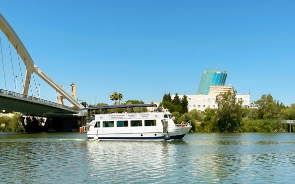 Sightseeing cruise boat on Guadalquivir River near bridge in Seville, Spain.