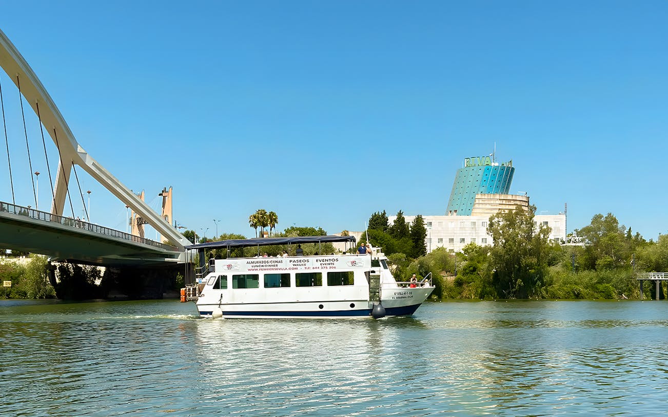 Sightseeing cruise boat on Guadalquivir River near bridge in Seville, Spain.
