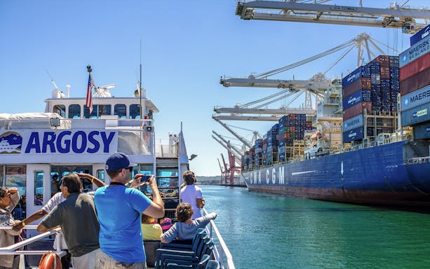 Tourists on a Seattle harbor cruise near cargo ships and cranes, part of Seattle C3® by CityPASS®.