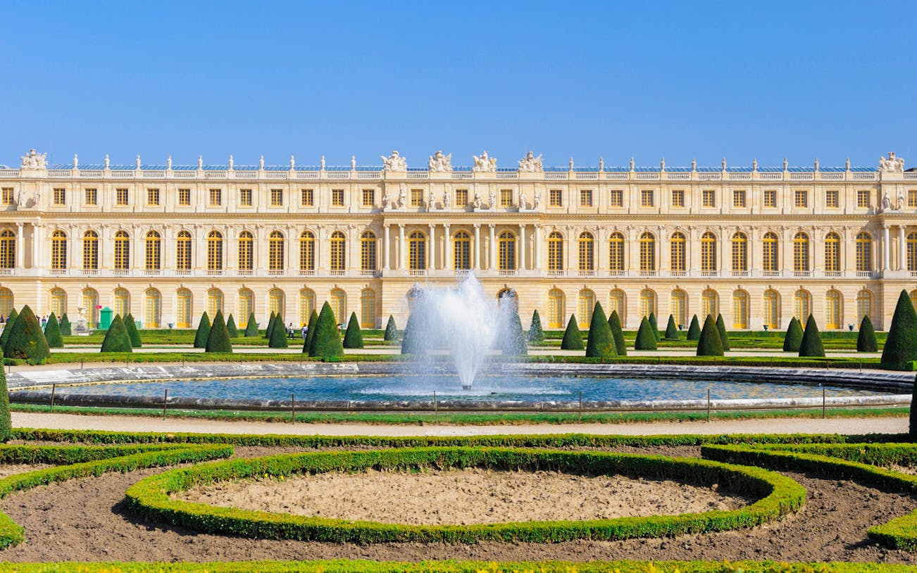 Palace of Versailles gardens with central fountain and manicured hedges in Paris.