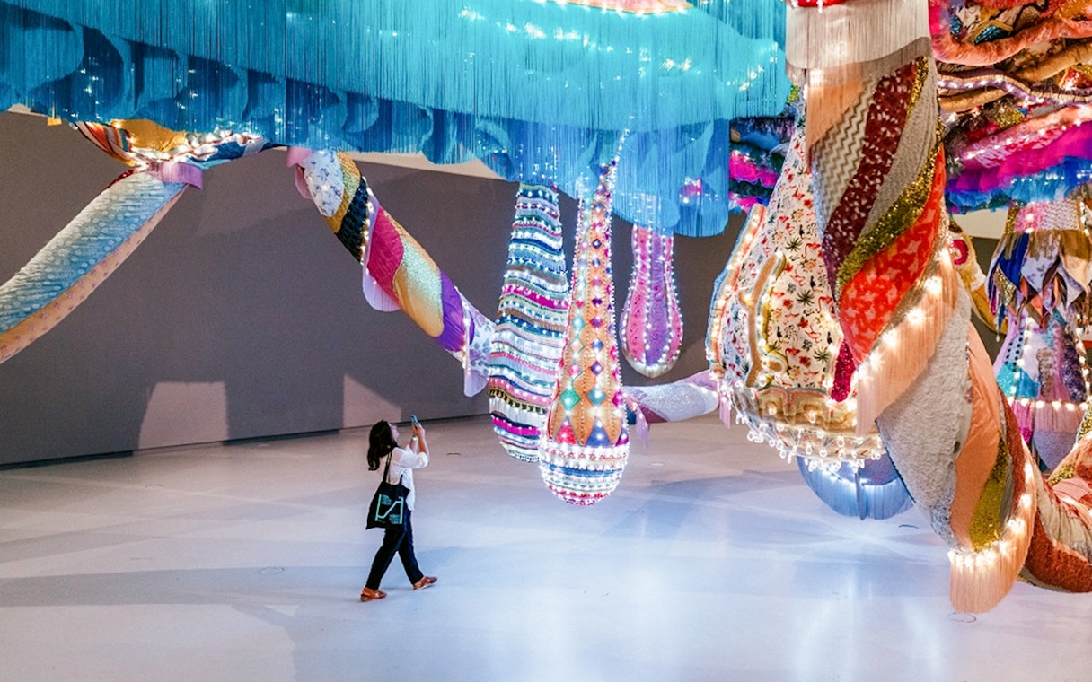 Colorful textile installation at MAAT Gallery with visitor taking a photo.