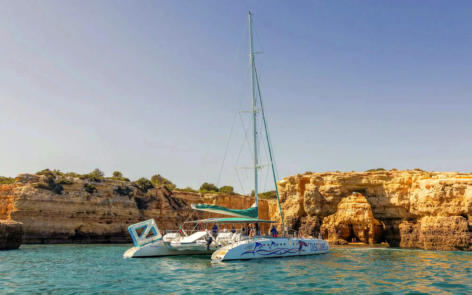 Catamaran near Algarve cliffs during sunset boat experience with drinks.