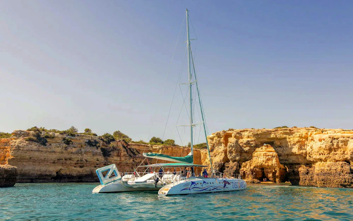 Catamaran near Algarve cliffs during sunset boat experience with drinks.