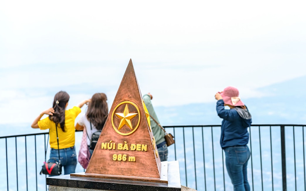 Ba Den mountain summit marker with tourists enjoying the view.