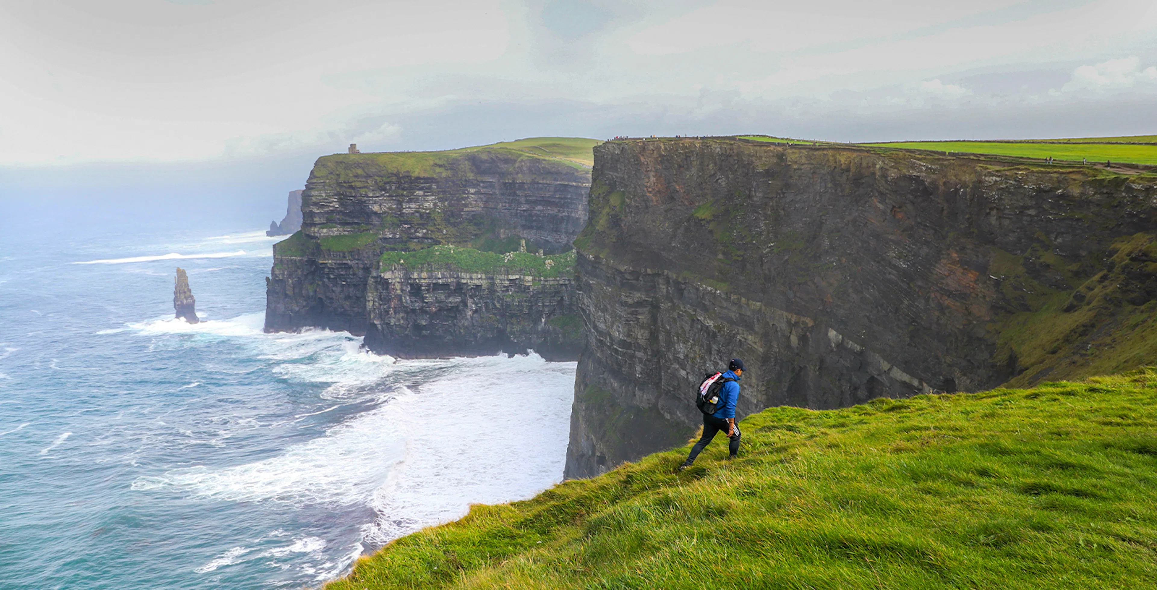 Hiker walking along the Cliffs of Moher in Ireland with ocean view.