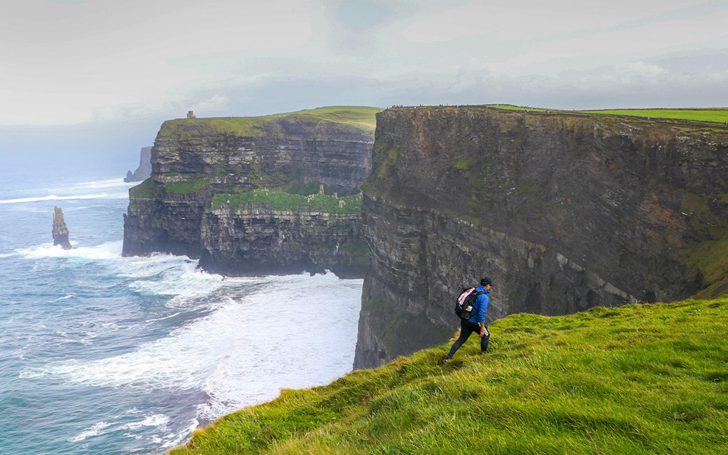 Hiker walking along the Cliffs of Moher in Ireland with ocean view.