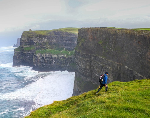 Hiker walking along the Cliffs of Moher in Ireland with ocean view.