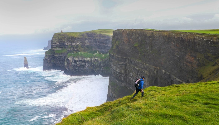 Hiker walking along the Cliffs of Moher in Ireland with ocean view.