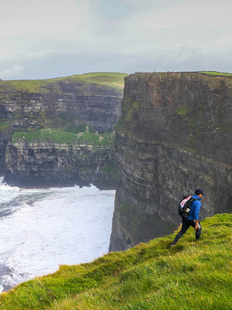 Hiker walking along the Cliffs of Moher in Ireland with ocean view.