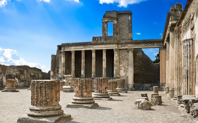 Pompeii Basilica ruins with ancient columns under a clear blue sky.