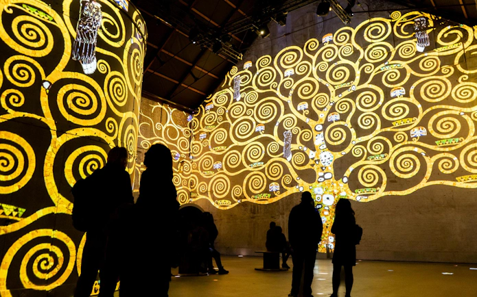 Visitors viewing illuminated art projections at Fabrique des Lumières, featuring swirling patterns.