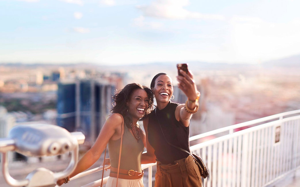Two people taking a selfie on a Las Vegas observation deck with city view.