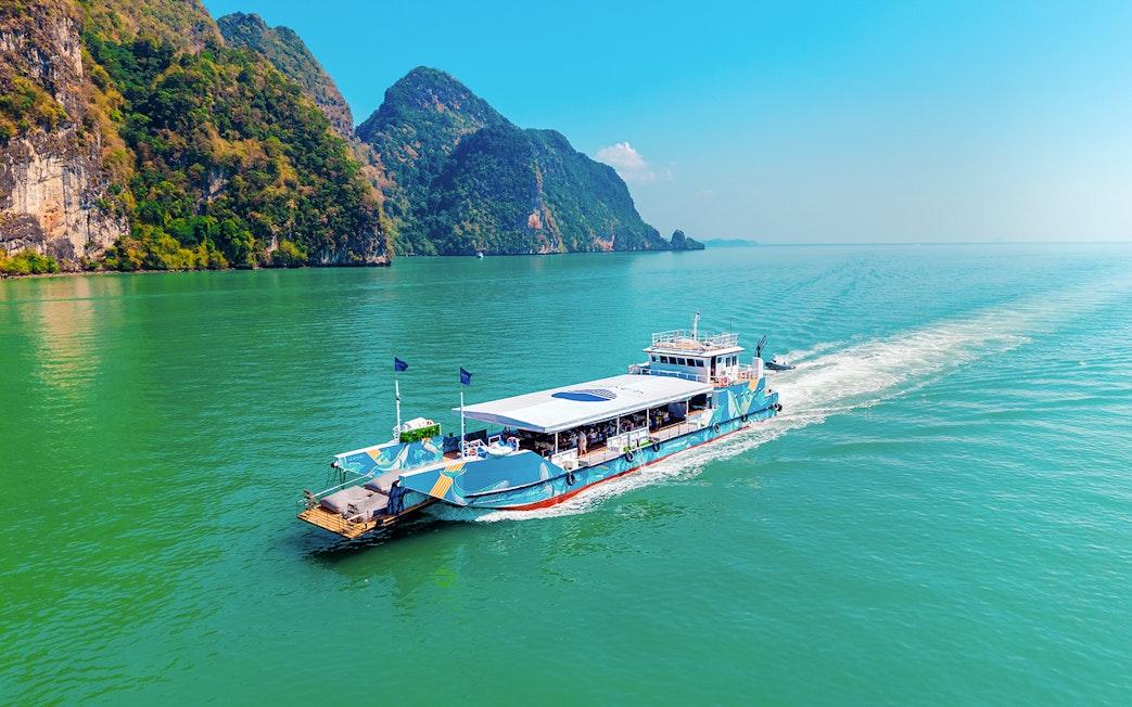 Cruise boat sailing in Phang Nga Bay with limestone cliffs in the background.