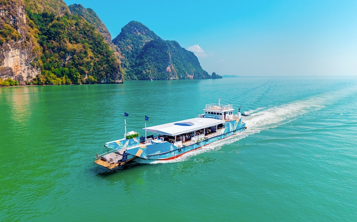 Cruise boat sailing in Phang Nga Bay with limestone cliffs in the background.